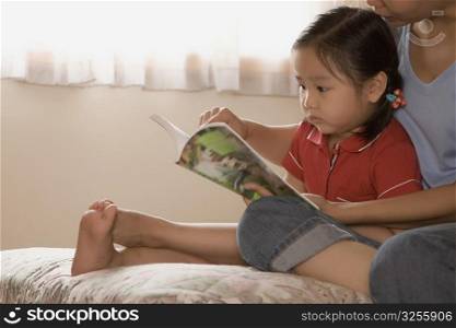 Close-up of a girl sitting with her mother and reading a book