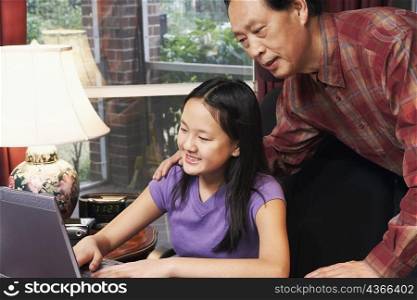 Close-up of a girl using a laptop with her father behind her