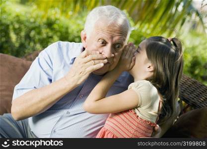 Close-up of a girl whispering into her grandfather&acute;s ear