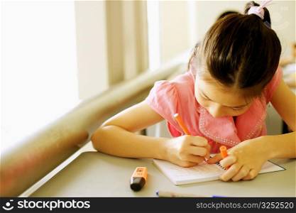Close-up of a girl writing on a spiral notebook in the classroom