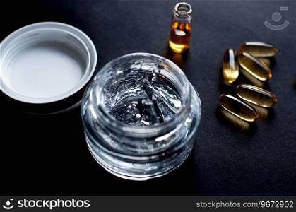Close-up of a glass jar of cosmetic gel and a bottle of oil on a black background