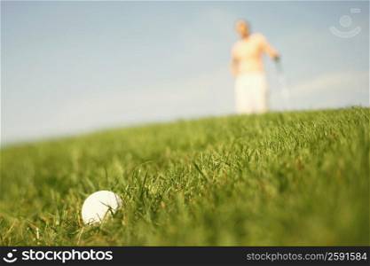 Close-up of a golf ball in grass with a woman in the background