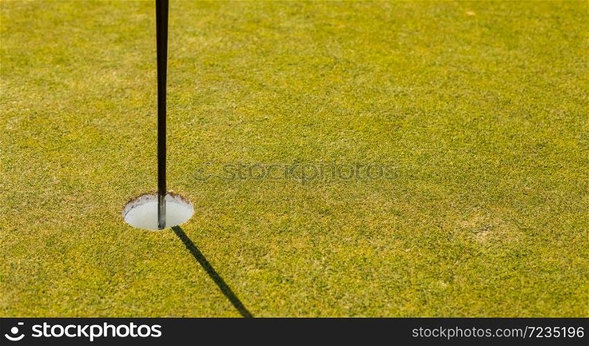 Close up of a golf course putting green hole with flag pole in afternoon light with shadow