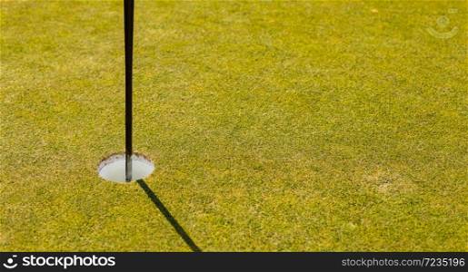 Close up of a golf course putting green hole with flag pole in afternoon light with shadow
