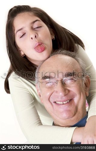 Close-up of a granddaughter sticking out her tongue and hugging her grandfather