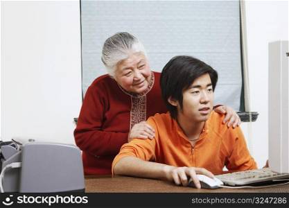 Close-up of a grandson using a computer with his grandmother standing behind him