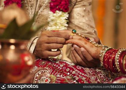 Close-up of a groom putting a wedding ring on a bride