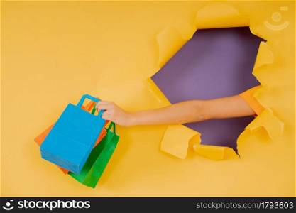Close-up of a hand holding shopping bags through a hole in paper wall. Shop concept.