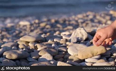 Close-up of a hand making a stone pyramid on pebble beach. Motion blur of water in background.