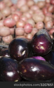 Close-up of a heap of eggplants with onions in the background