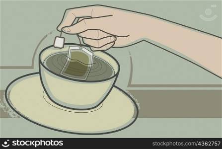 Close-up of a human hand dipping teabag in a tea cup
