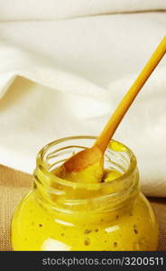 Close-up of a jar of mustard with a wooden spoon
