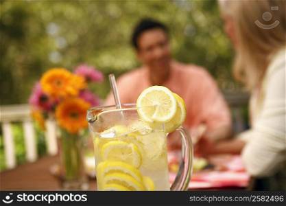 Close-up of a jug of lemon juice with two people sitting in the background