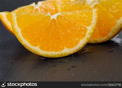 Close up of a juicy slice of orange fruit, resting on skin side, with natural slate stone underneath. Selective focus on front part of fruit.