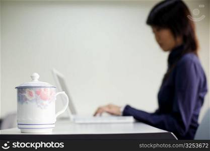Close-up of a kettle and a young woman using a laptop