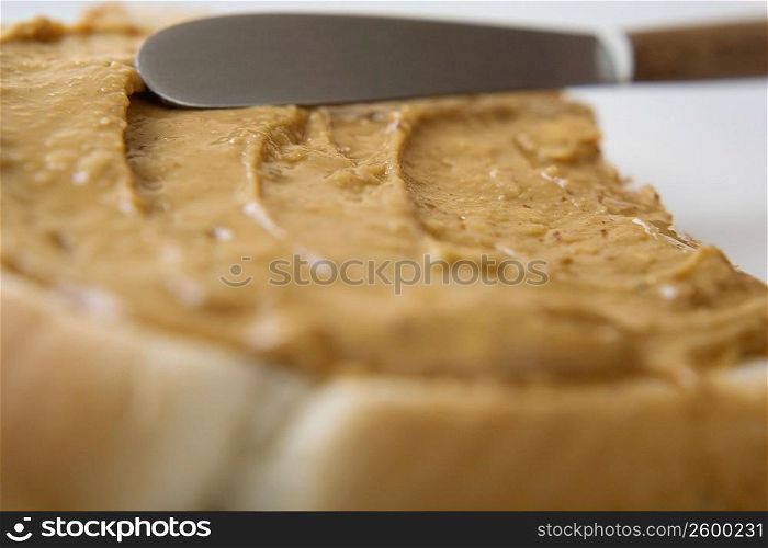 Close-up of a knife spreading peanut butter on a slice of bread