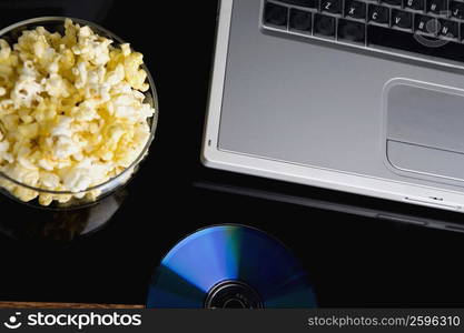 Close-up of a laptop with a bowl of popcorn and a CD