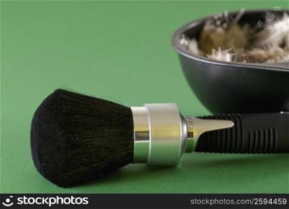 Close-up of a make-up brush with a bowl of feathers beside it