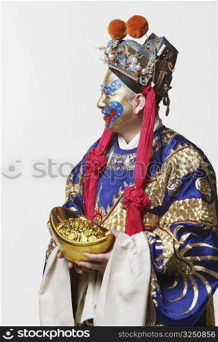 Close-up of a male Chinese opera performer holding a bowl full of gold coins