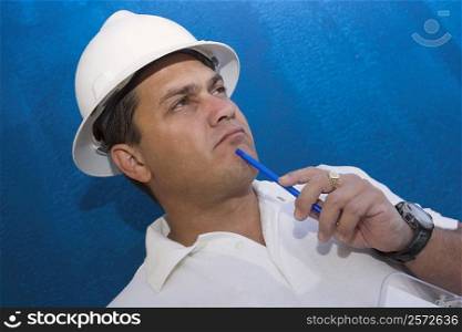 Close-up of a male construction worker holding a pen and thinking