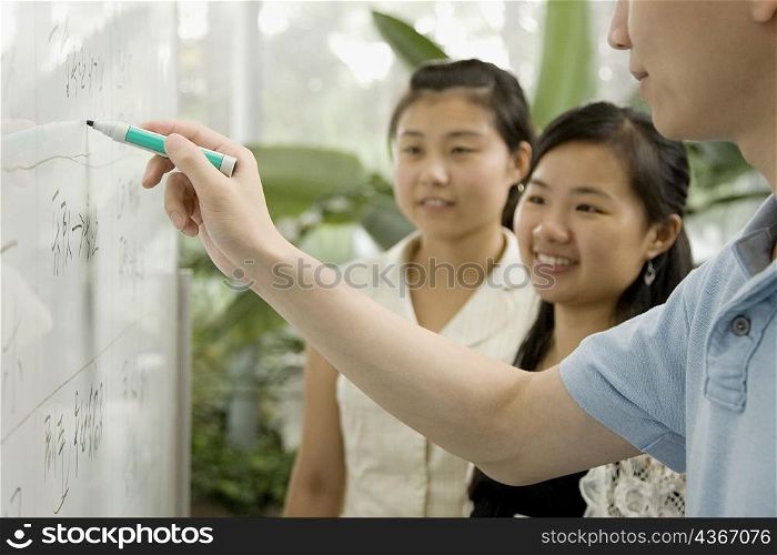 Close-up of a male office worker writing on a whiteboard and two female office workers looking on it