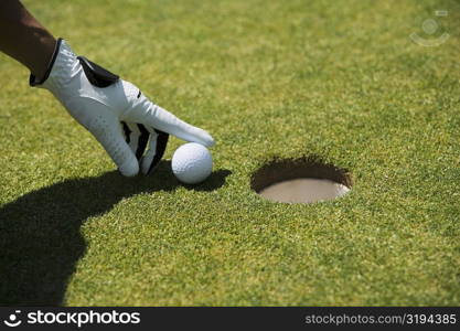 Close-up of a man&acute;s hand putting a golf ball near a hole