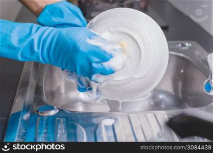 Close up of a man wearing a blue rubber glove was washing the cup with a dish washing liquid in the sink in the kitchen.