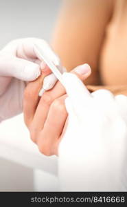 Close up of a manicurist files the female nails with the nail file in a nail salon. Manicurist filing the female nails