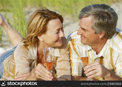 Close-up of a mature couple lying on the beach and holding champagne flutes