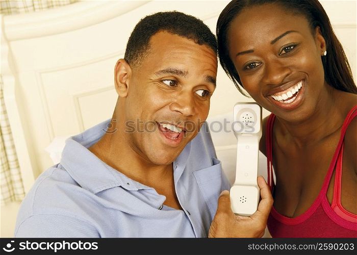 Close-up of a mature man and a mid adult woman listening to a telephone receiver and smiling