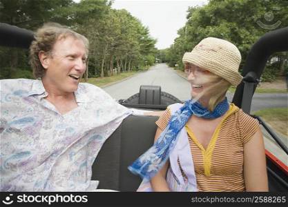 Close-up of a mature man and a mid adult woman sitting in a convertible car and smiling