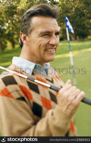 Close-up of a mature man carrying a golf club and smiling at a golf course