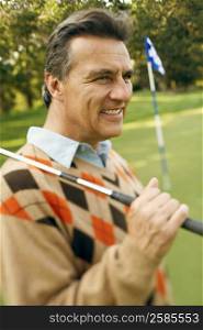 Close-up of a mature man carrying a golf club and smiling at a golf course