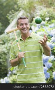 Close-up of a mature man holding a croquet mallet and tossing a ball