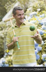 Close-up of a mature man holding a croquet mallet and tossing a ball