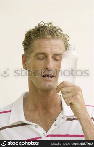 Close-up of a mature man holding a water bottle with his eyes closed