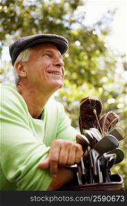 Close-up of a mature man leaning on a golf bag and smiling