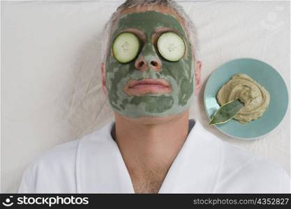 Close-up of a mature man lying down with a face pack and cucumber slices on her eyes