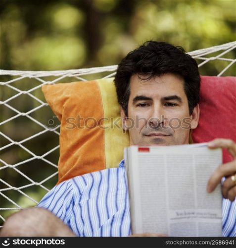 Close-up of a mature man lying in a hammock and reading a magazine