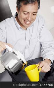 Close-up of a mature man pouring coffee into a mug from a kettle