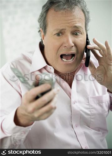 Close-up of a mature man shouting on a mobile phone and holding two mobile phones in his other hand