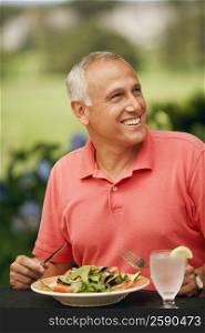 Close-up of a mature man sitting at the table with a plate of vegetable salad in front of him