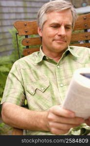 Close-up of a mature man sitting on a chair and reading a book