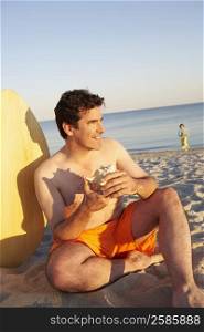 Close-up of a mature man sitting on the beach and holding a seashell