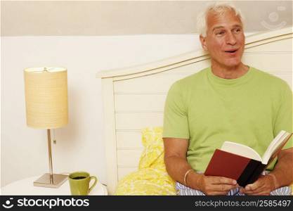 Close-up of a mature man sitting on the bed and holding a book