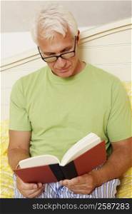 Close-up of a mature man sitting on the bed and reading a book