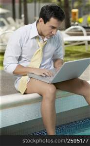 Close-up of a mature man sitting on the ledge and using a laptop