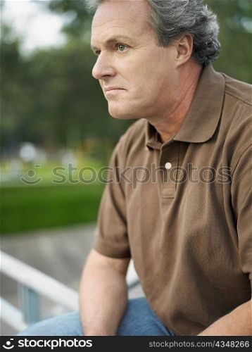 Close-up of a mature man sitting on the railing in a park