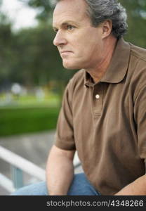 Close-up of a mature man sitting on the railing in a park