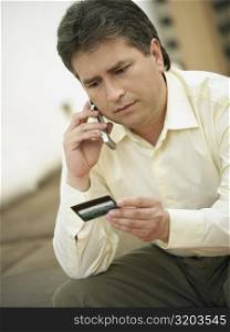 Close-up of a mature man talking on a mobile phone and holding a credit card